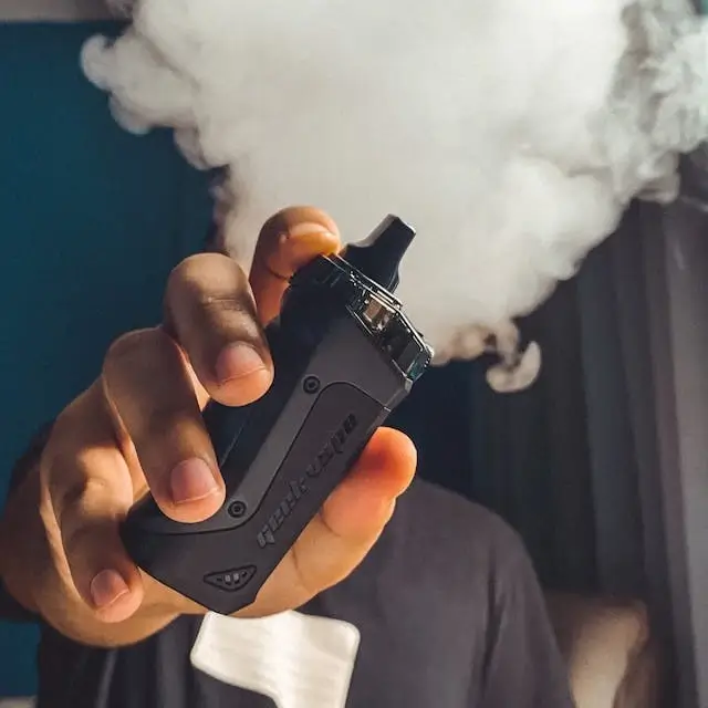 Hand holding some vape hardware (a starter kit mod vape) in front of a cloud of vapor.